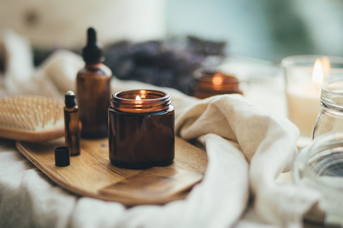 Bath oils, herbal bottles and a lit candle on a wooden tray by the bath