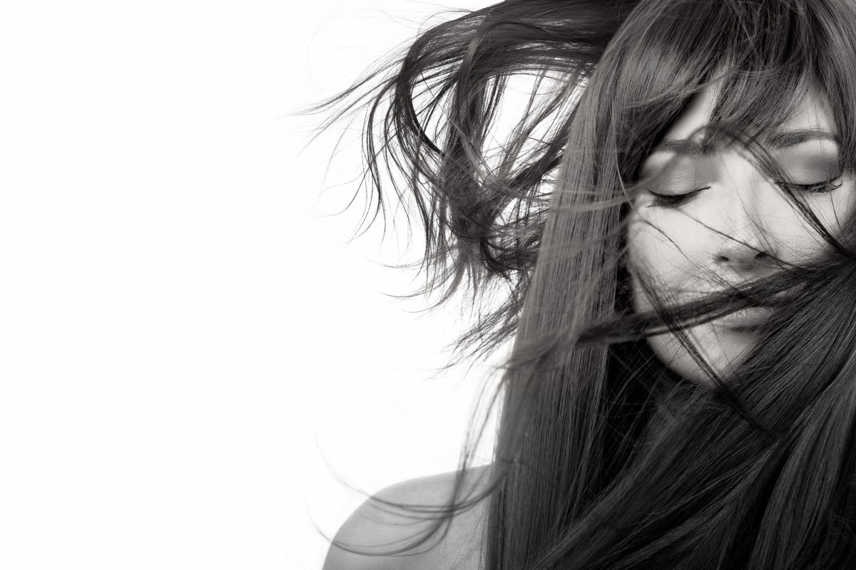 A black and white portrait of a woman with long, healthy hair moving in the air