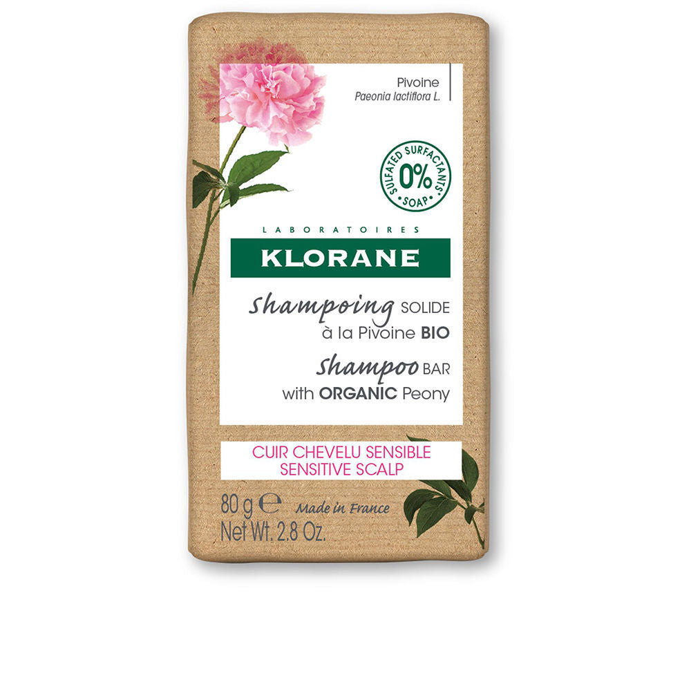 Klorane Brown rectangular shampoo bar in kraft paper with pink peony illustration, green accents, text labels, organic mark