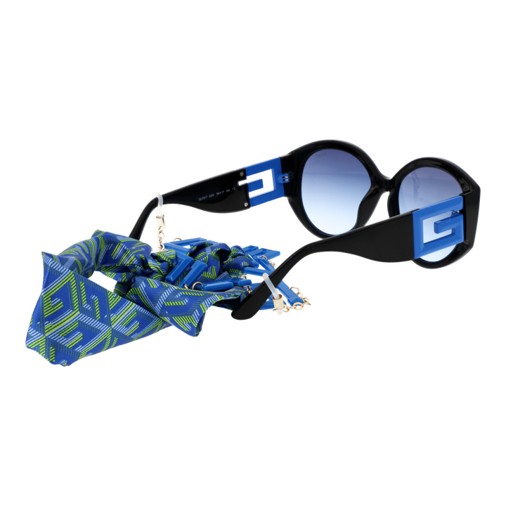 Black cat-eye sunglasses with gradient blue lenses, blue-green patterned scarf and gold chain charms